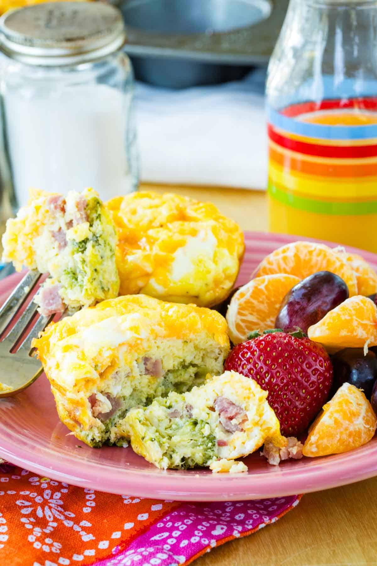 Two egg muffins on a plate with one that has been cut into alongside fruit.