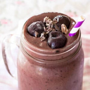 The top of a chocolate cherry smoothie in a glass jar topped with frozen cherries and cacao nibs.