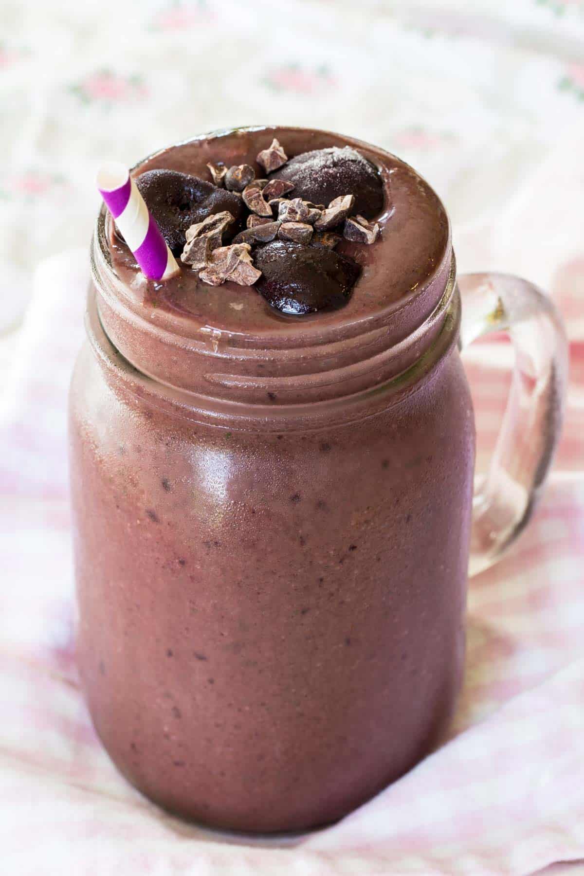 Chocolate cherry smoothie topped with cacao nibs and cherries in a mason jar.