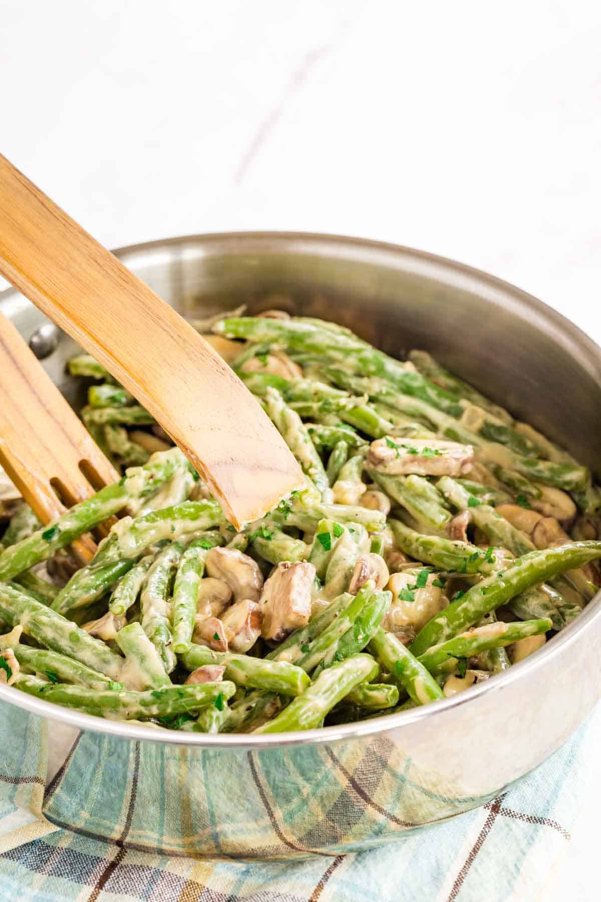 Tongs picking up creamy green beans and mushrooms from a skillet.