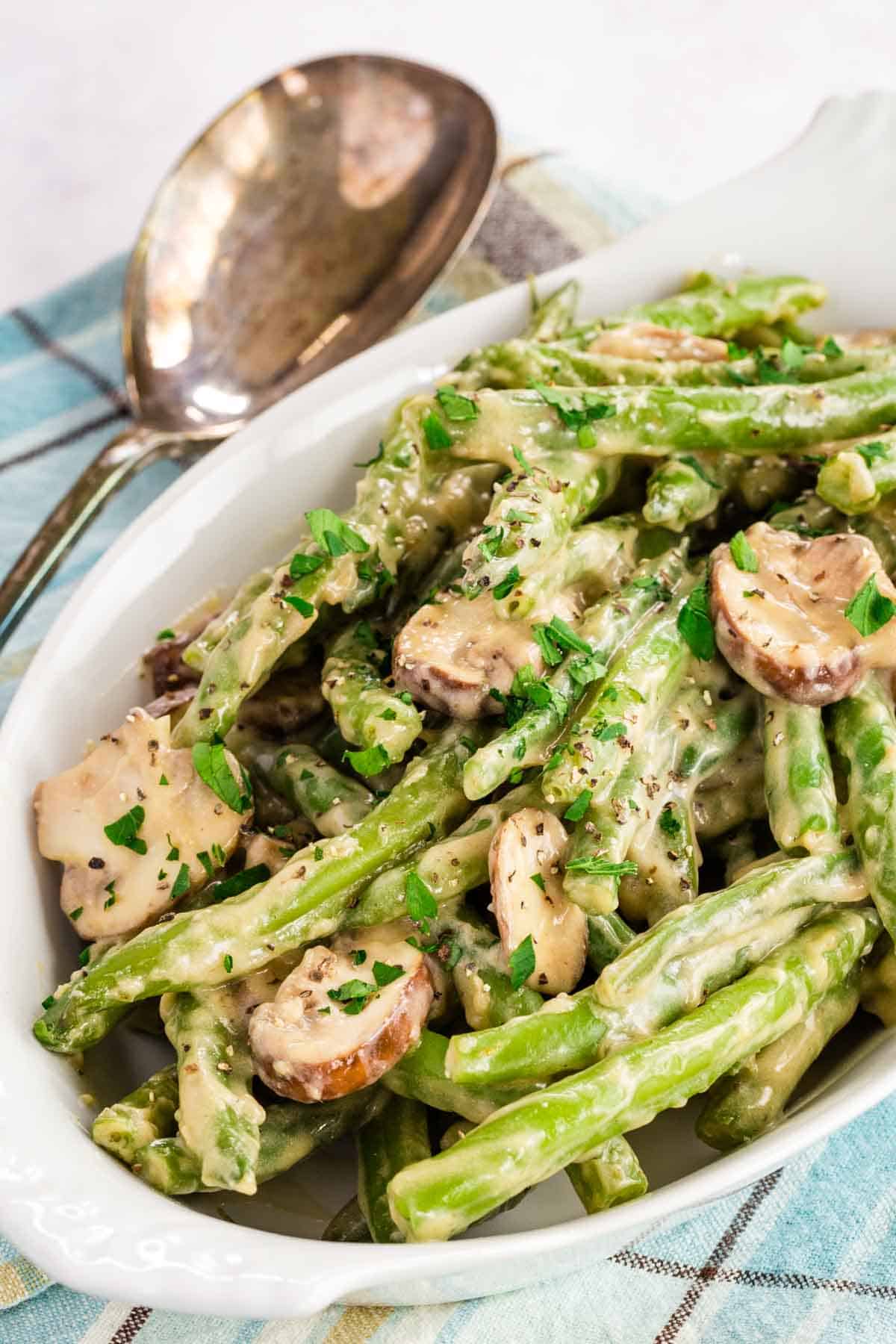 Creamy green beans mushrooms in a white oval dish with a serving spoon next to it.