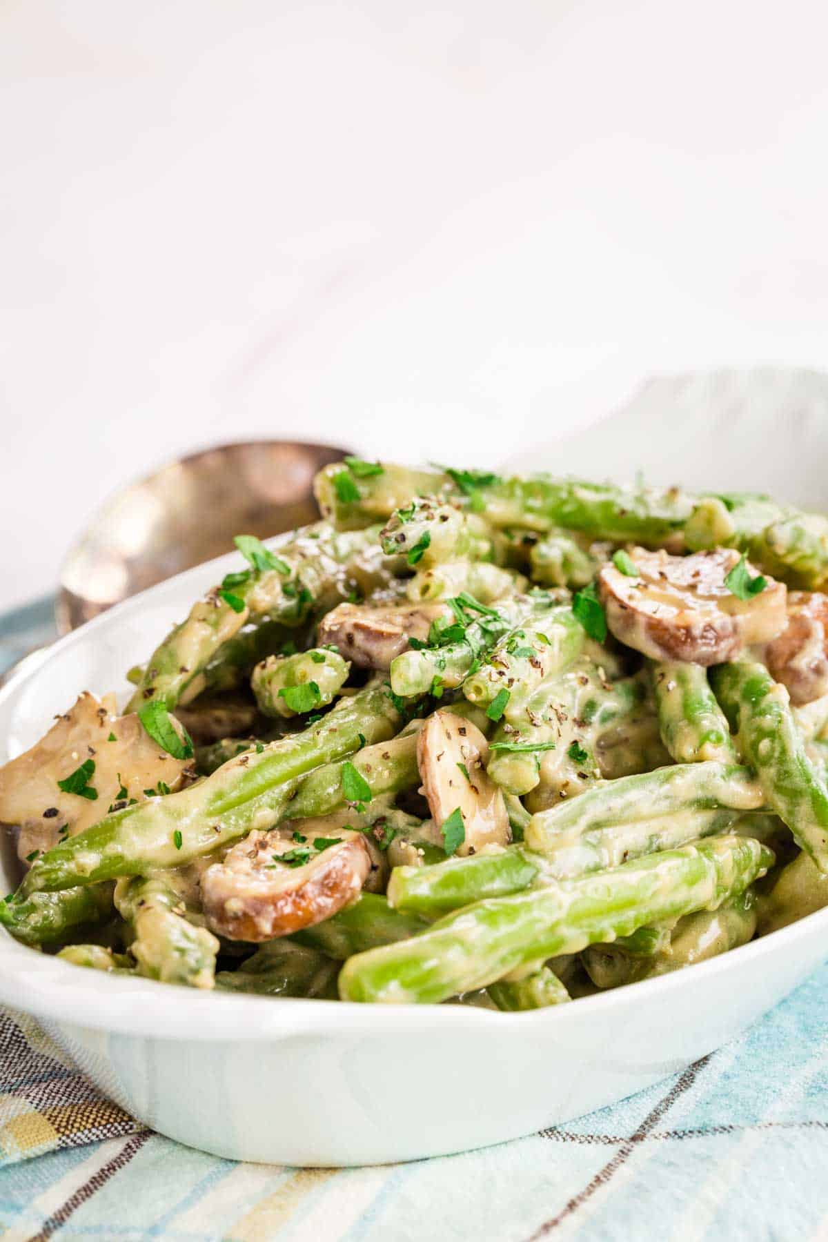 A close-up of green beans and mushrooms with a creamy sauce in a serving dish.