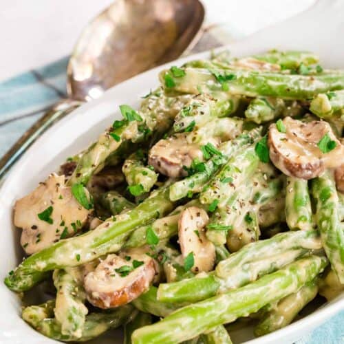 A dish of creamy green beans and mushrooms garnished with parsley.