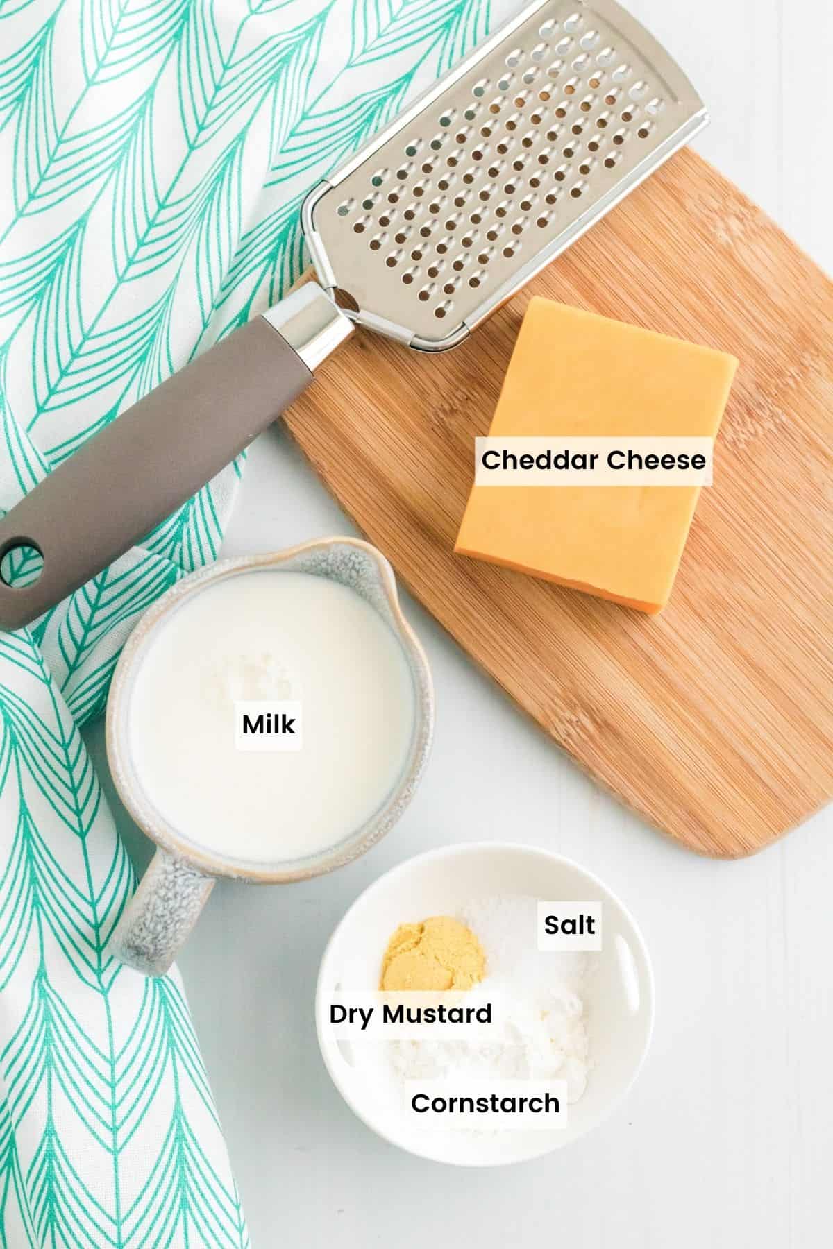 The 5 ingredients for gluten free cheese sauce with text labels: cheddar cheese, milk, dry mustard, cornstarch, and salt.