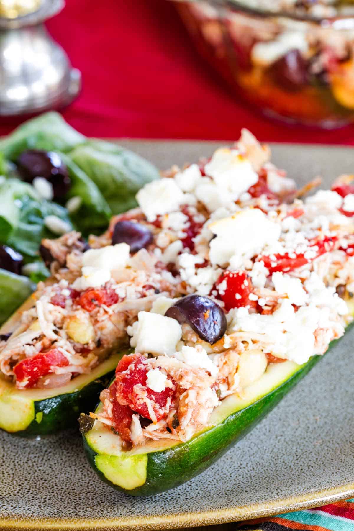 Two zucchini boats stuffed with shredded chicken tomatoes olives and feta cheese.