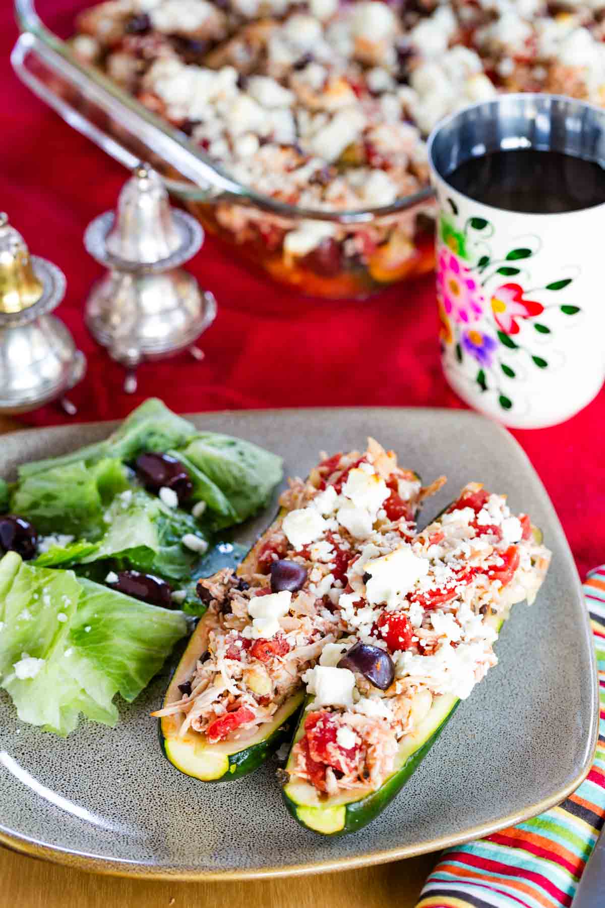 Two Greek chicken stuffed zucchini boats on a plate with a salad next to them.