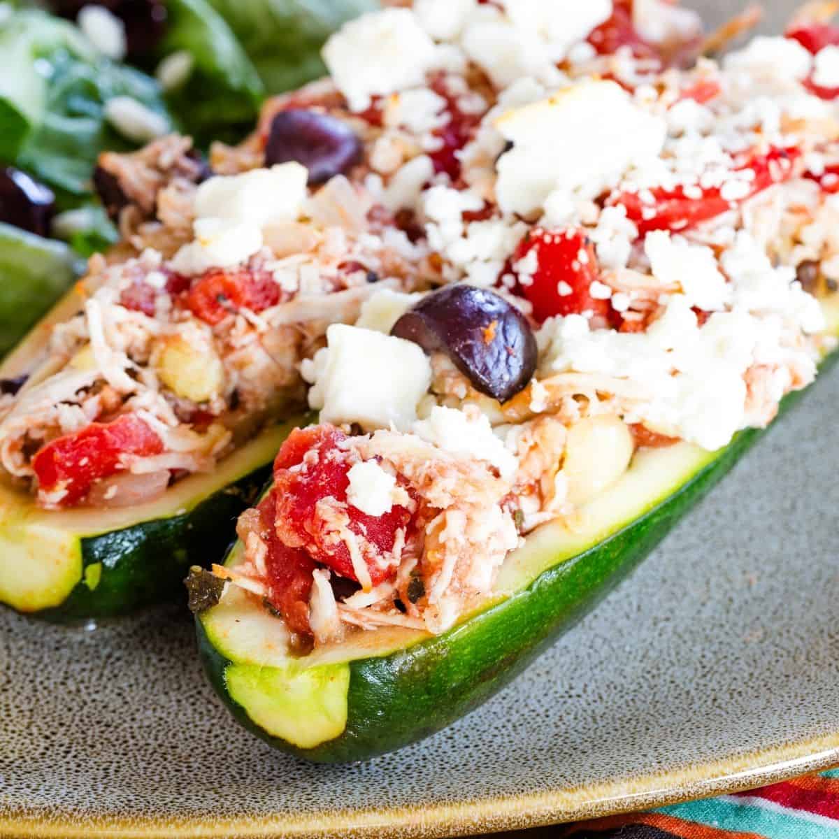 A close-up of two Greek chicken stuffed zucchini boat halves on a plate.