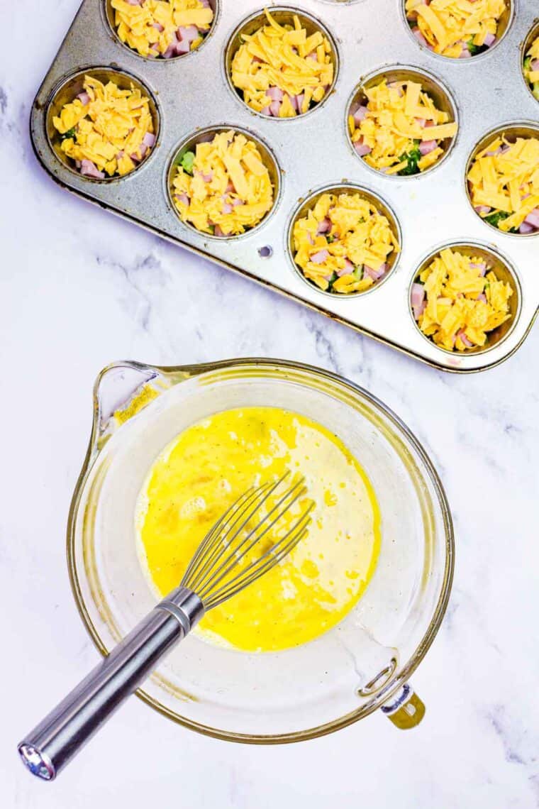 A whisk in a bowl of eggs that have been beaten.