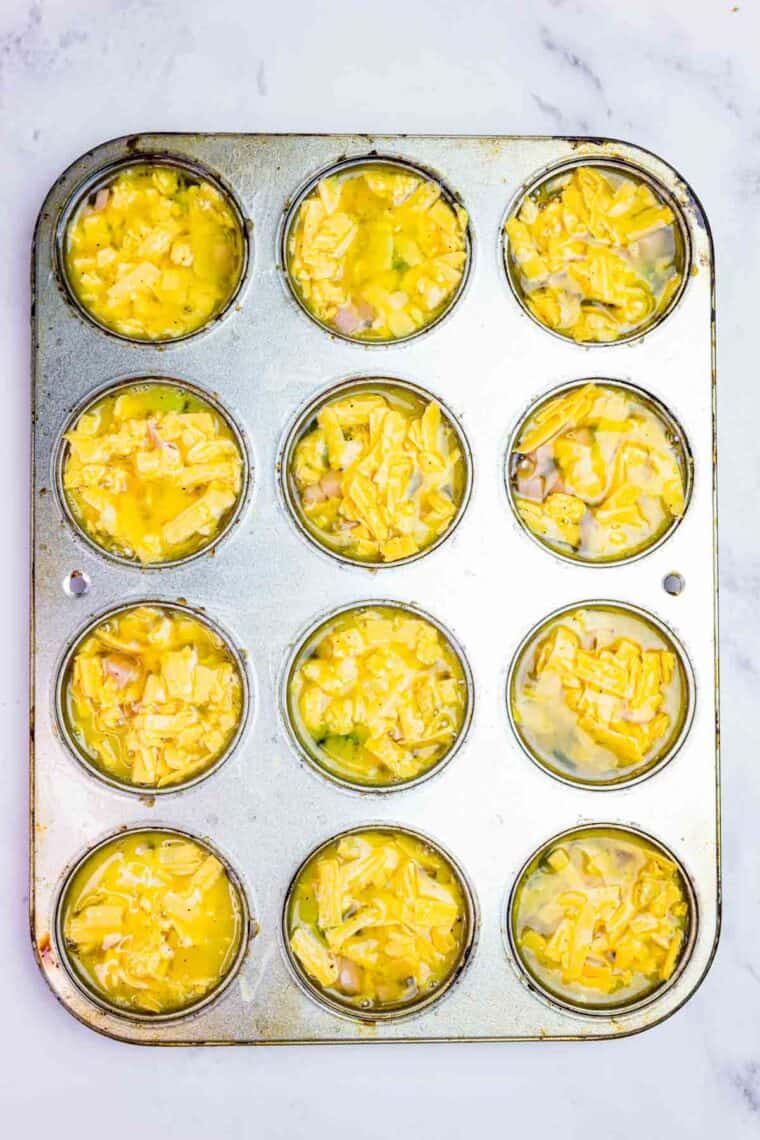 The uncooked egg, broccoli, ham and cheese mixture filling the muffin pan.