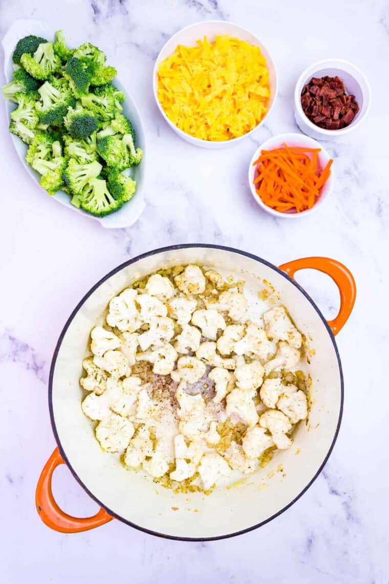 Cauliflower florets in a stockpot with other soup ingredients nearby in bowls.