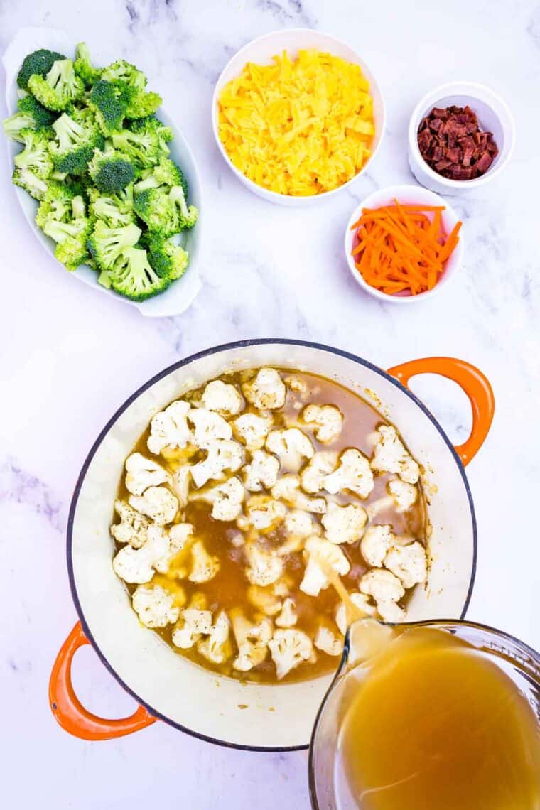 Chicken broth being added to the cauliflower in a pot.