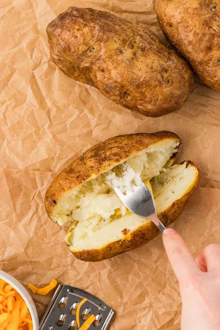 A fork fluffing the inside of a baked potato