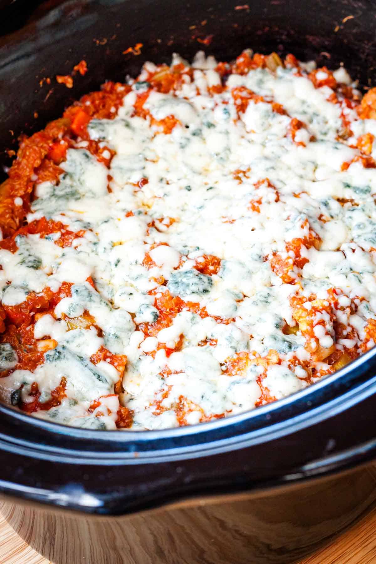Buffalo chicken quinoa topped with melted blue cheese in a crockpot.