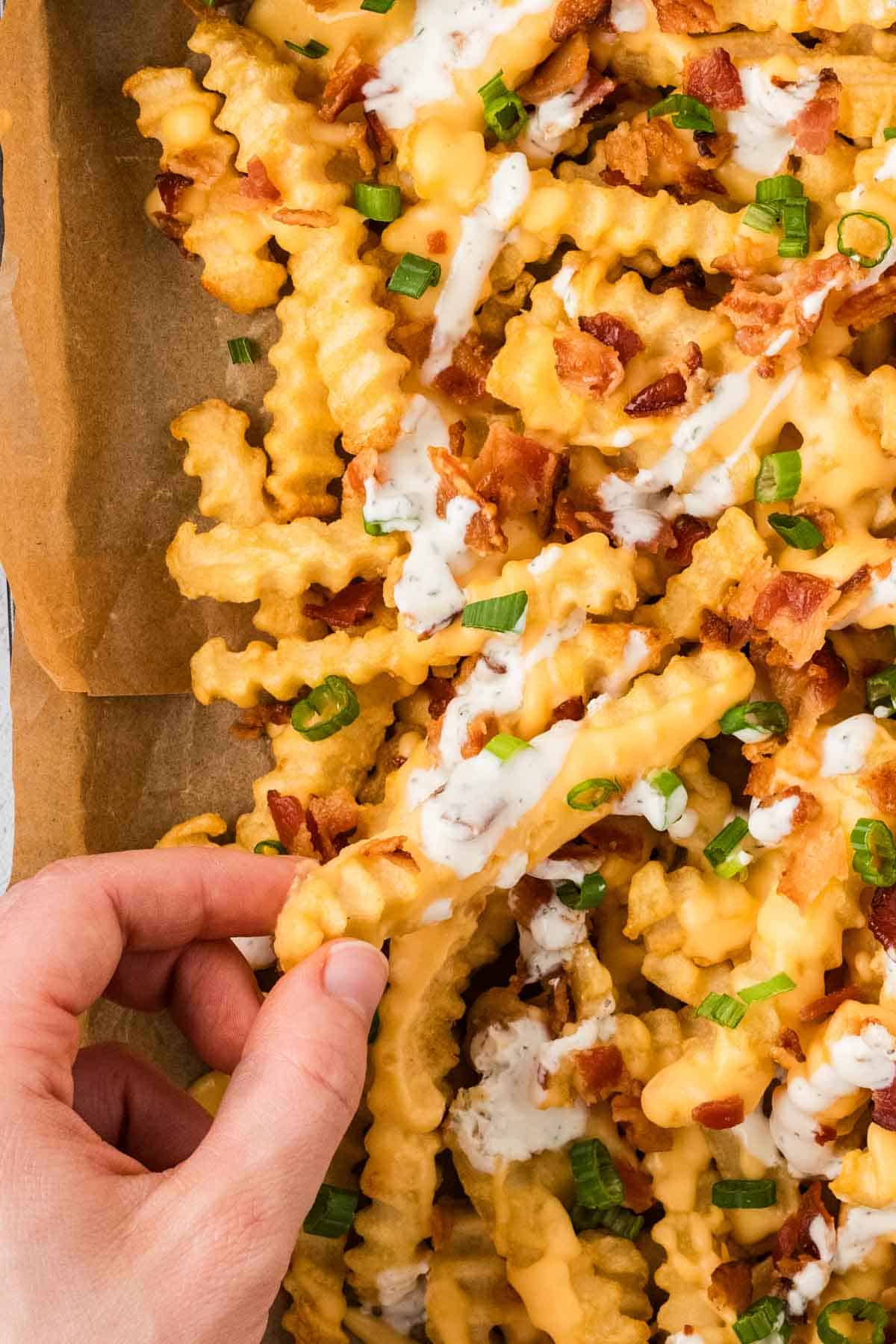 A hand holding a loaded fry over a baking sheet of them