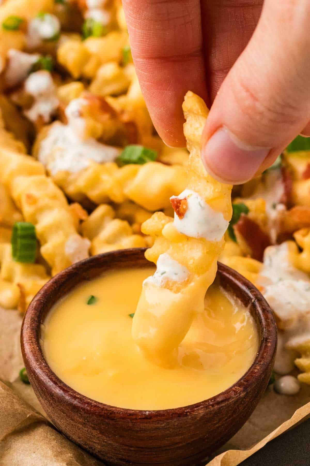 Close up of a hand dipping a fry into cheese sauce
