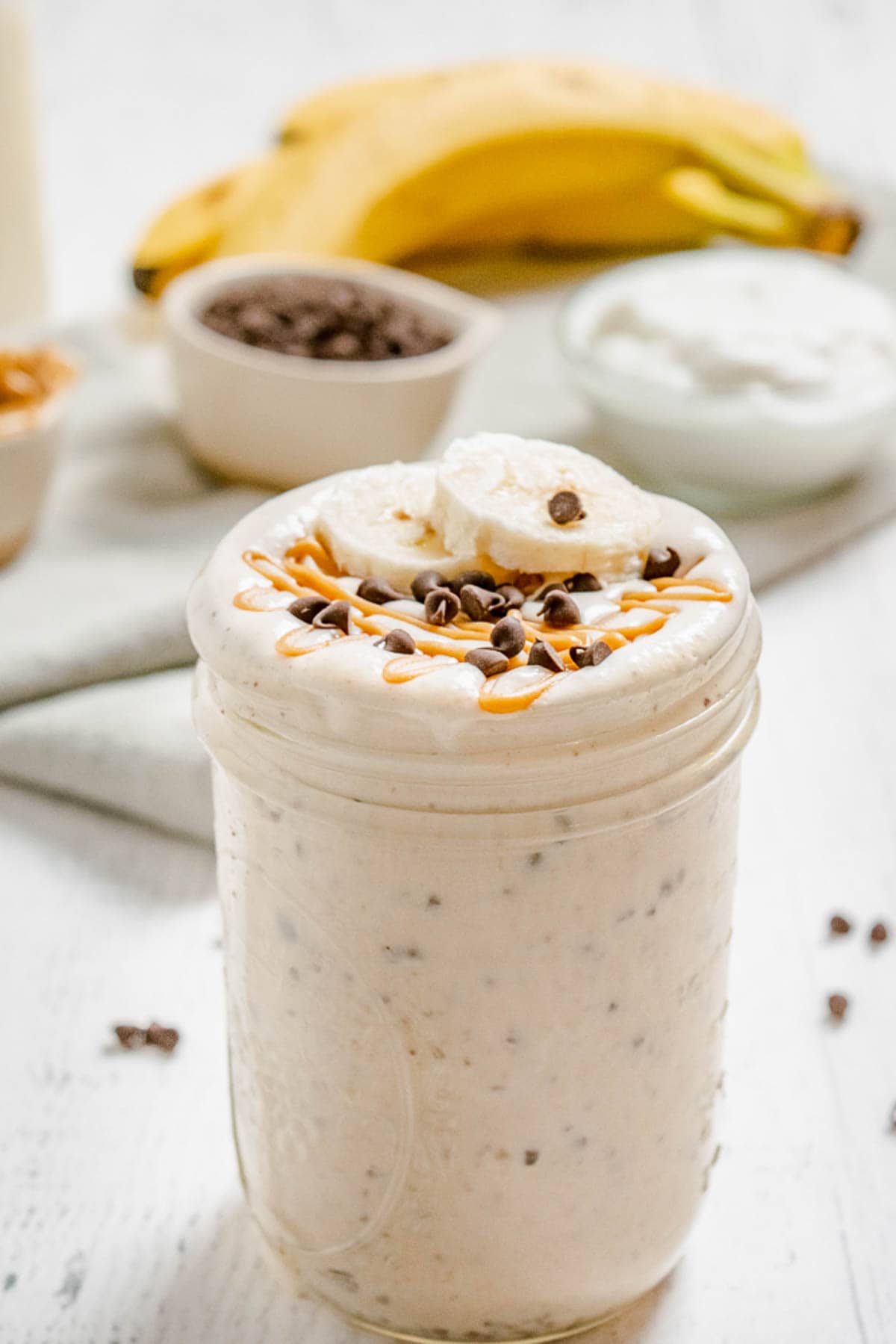 A peanut butter banana smoothie in a jar with mini chocolate chips blended into it.