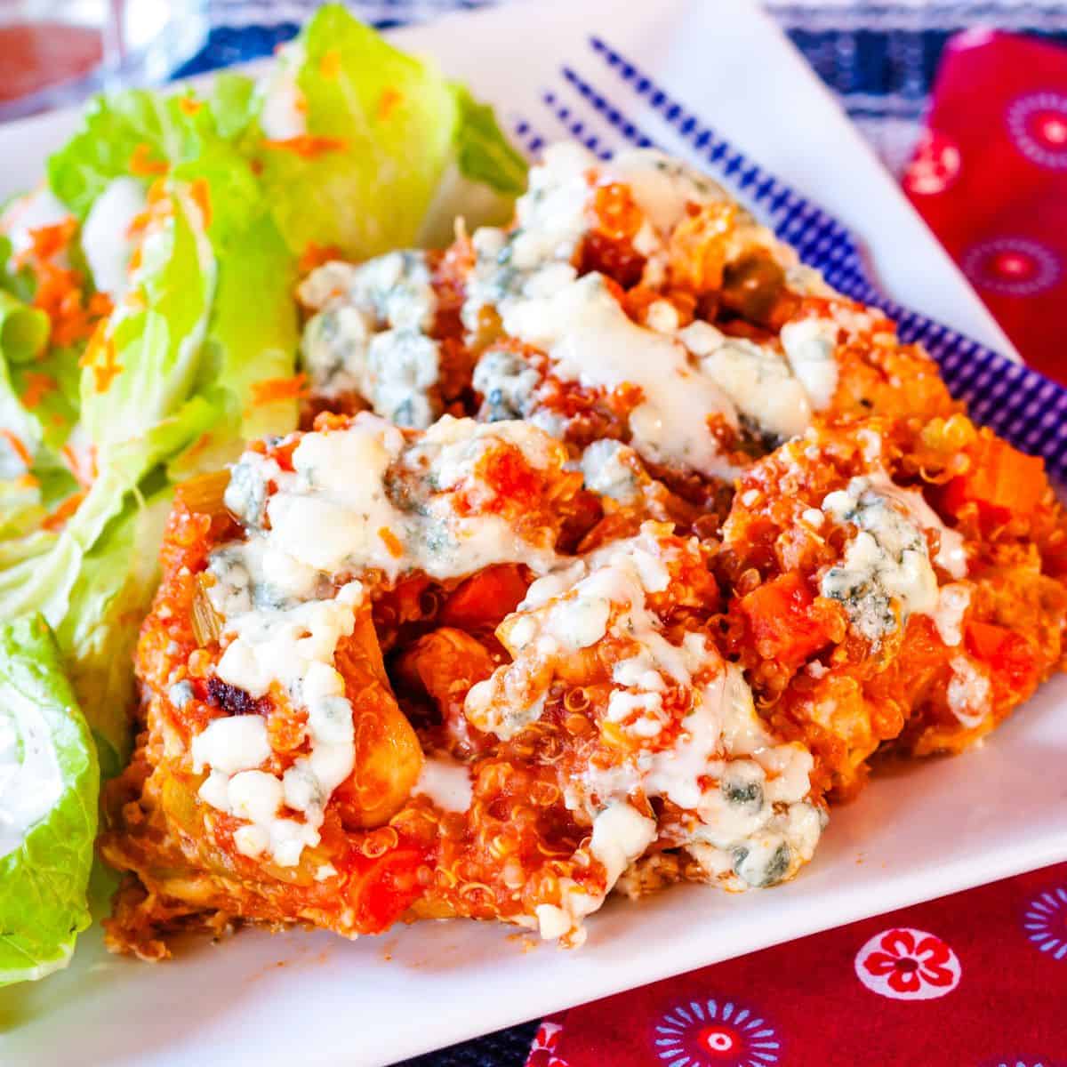 Buffalo chicken quinoa with blue cheese on top and it drizzle of ranch dressing on a white plate.