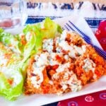 Buffalo chicken quinoa served with a salad on a white square plate.