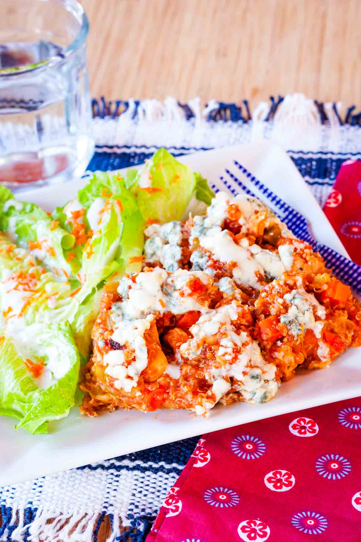 Buffalo chicken quinoa served with a salad on a white square plate.