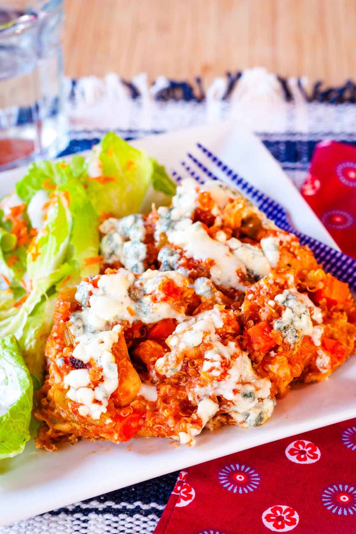 A serving of buffalo chicken quinoa topped with blue cheese and ranch dressing on a white plate.