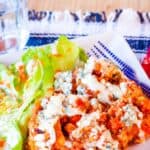 Saucy cooked quinoa topped with blue cheese on a plate with text overlay that says "Slow Cooker Buffalo Chicken Quinoa".