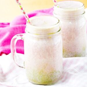 A swirled strawberry matcha smoothie in a glass jar with a handle and a floral straw.