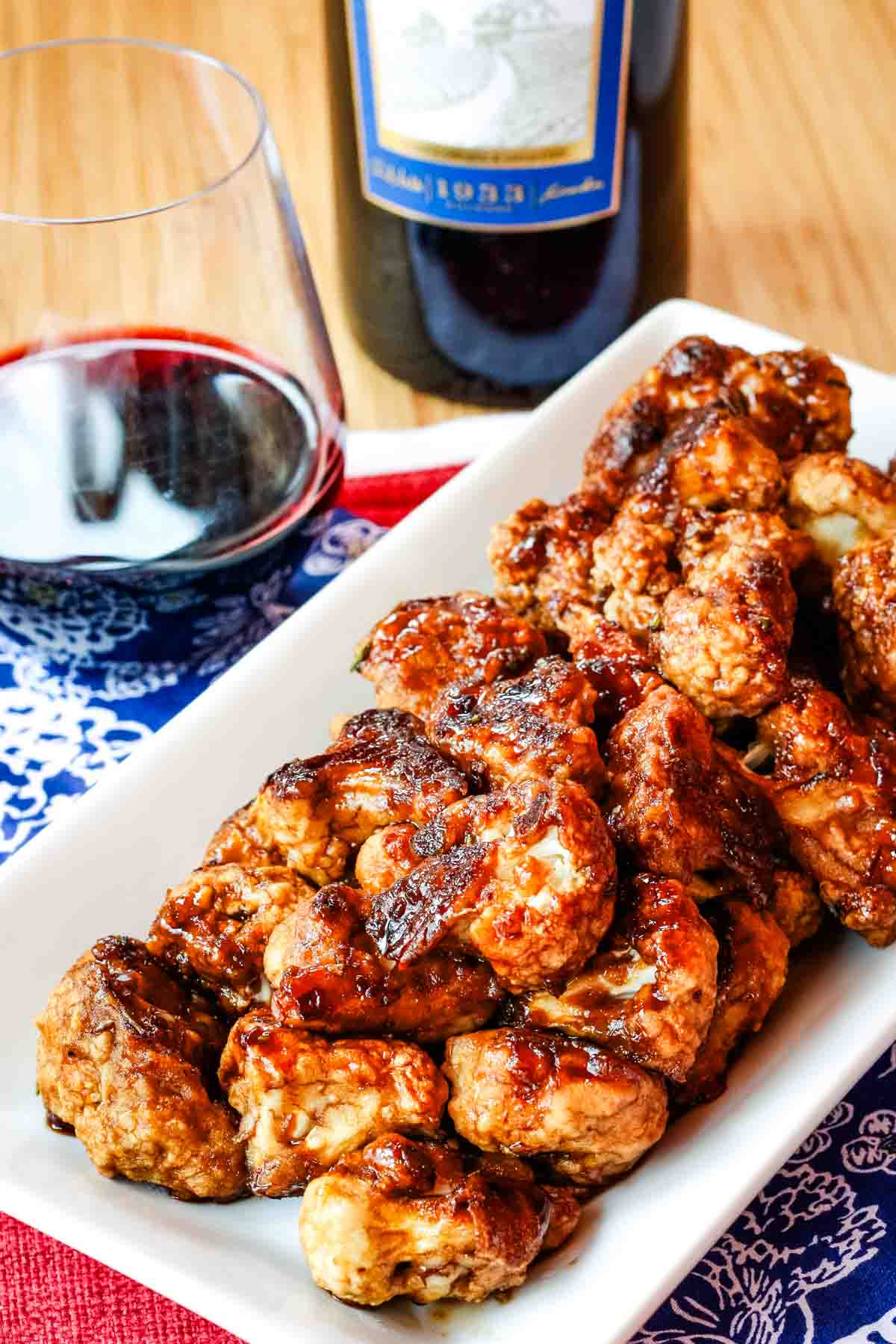 Balsamic cauliflower bites on a white dish with a glass and bottle of wine behind it.
