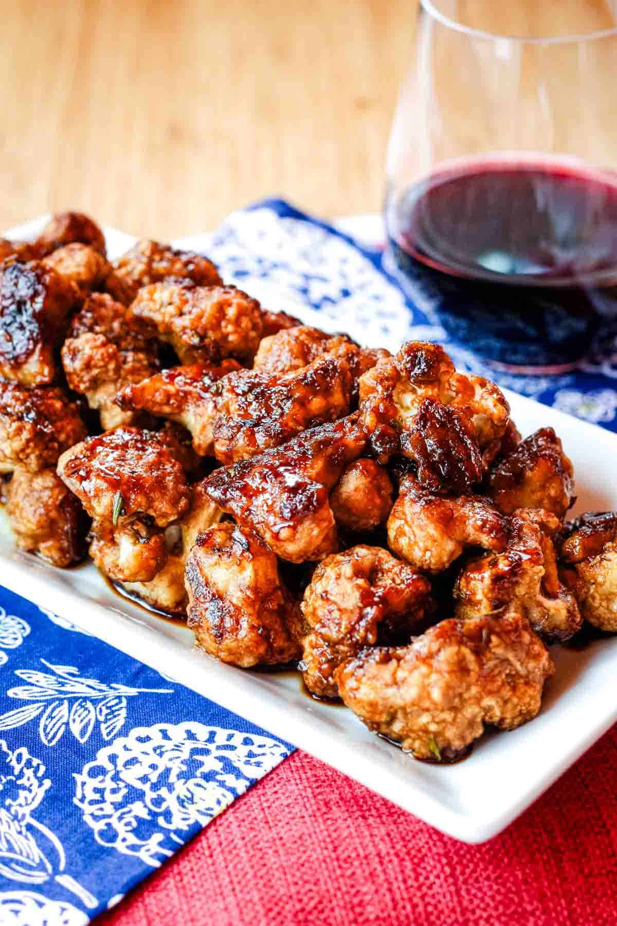 Glazed cauliflower florets on a white plate with a glass of wine in the background.