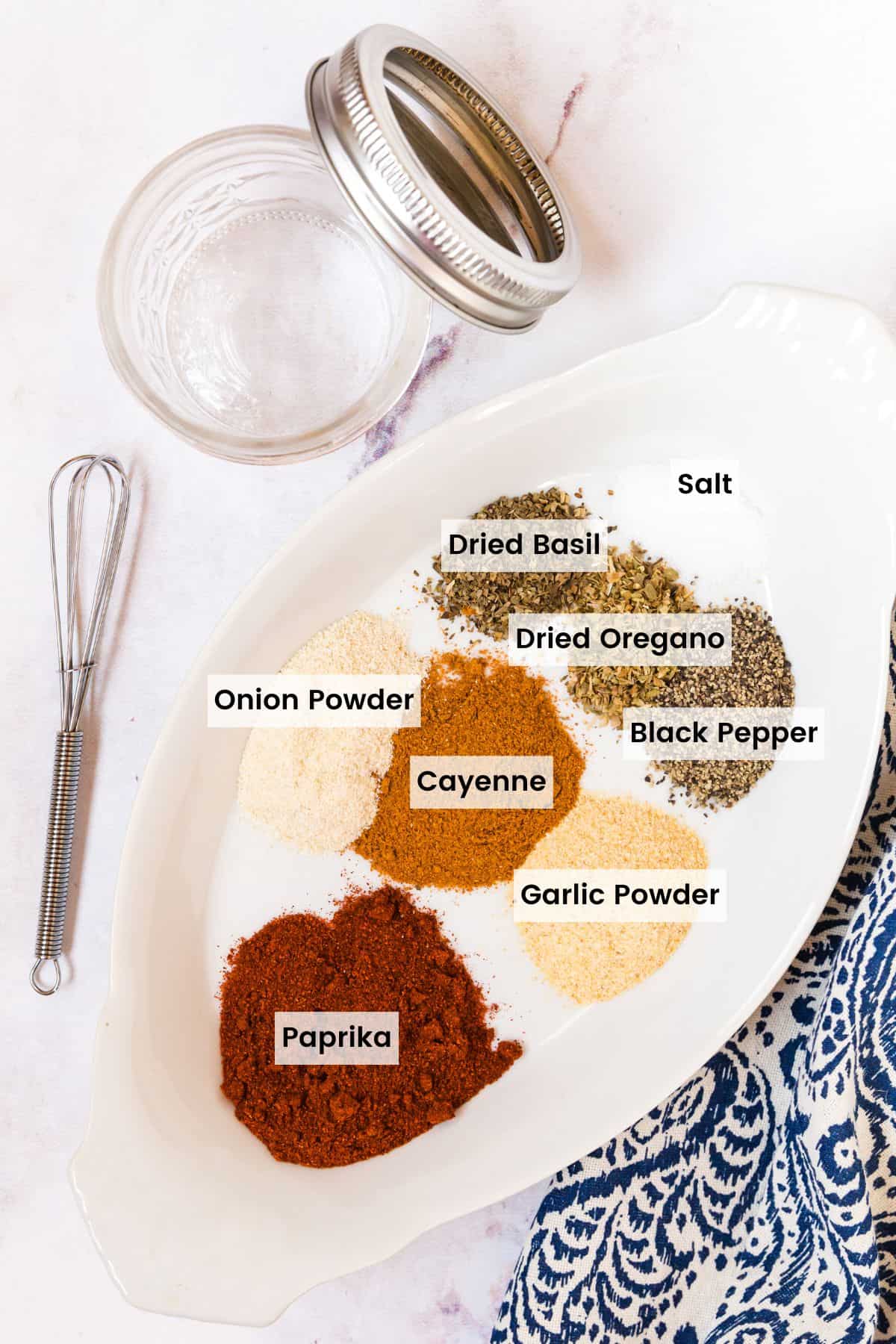 All of the dried herbs and spices for making a blackening seasoning mix in an oval dish each with a text label.