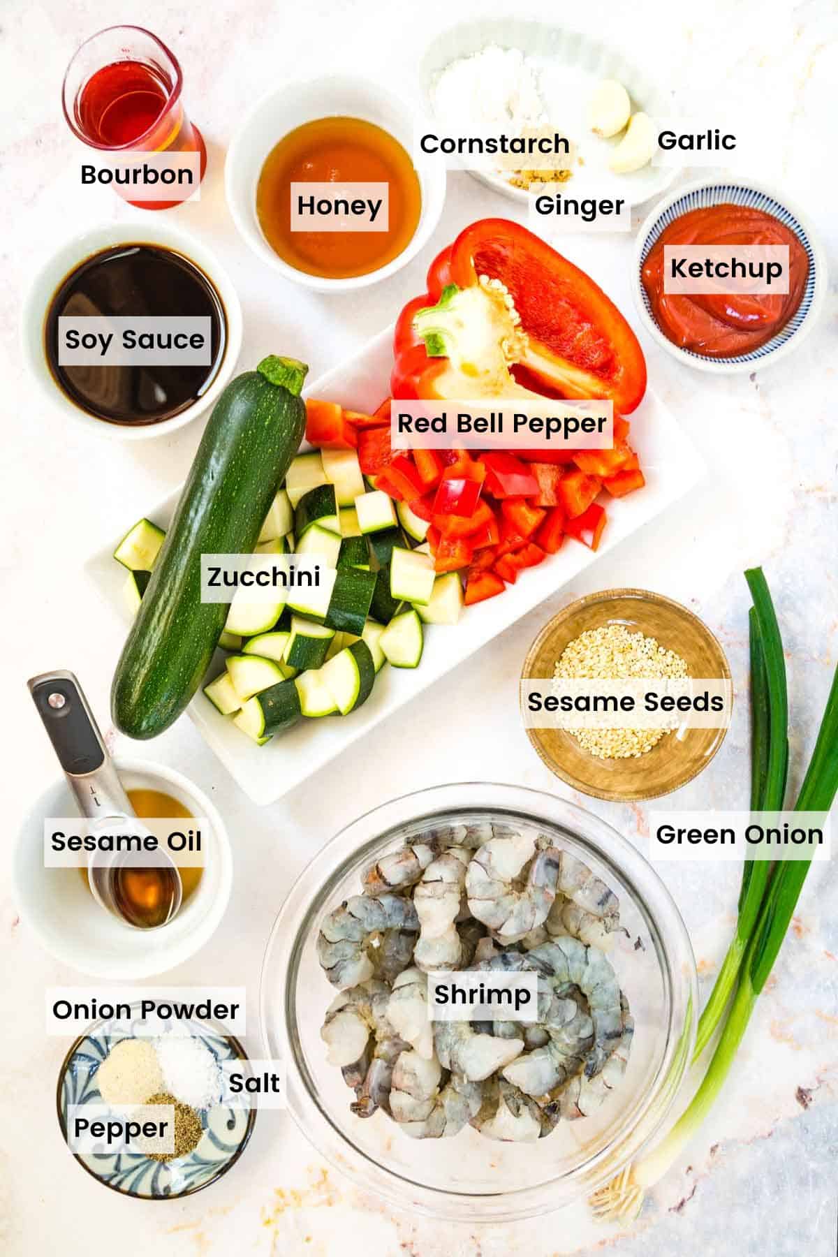 A bowl of raw shrimp, chopped zucchini and peppers, and bowls of other ingredients to make bourbon shrimp with text labels.