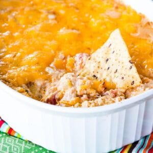 Tortilla chip resting in a baking dish of cheesy jambalaya dip.