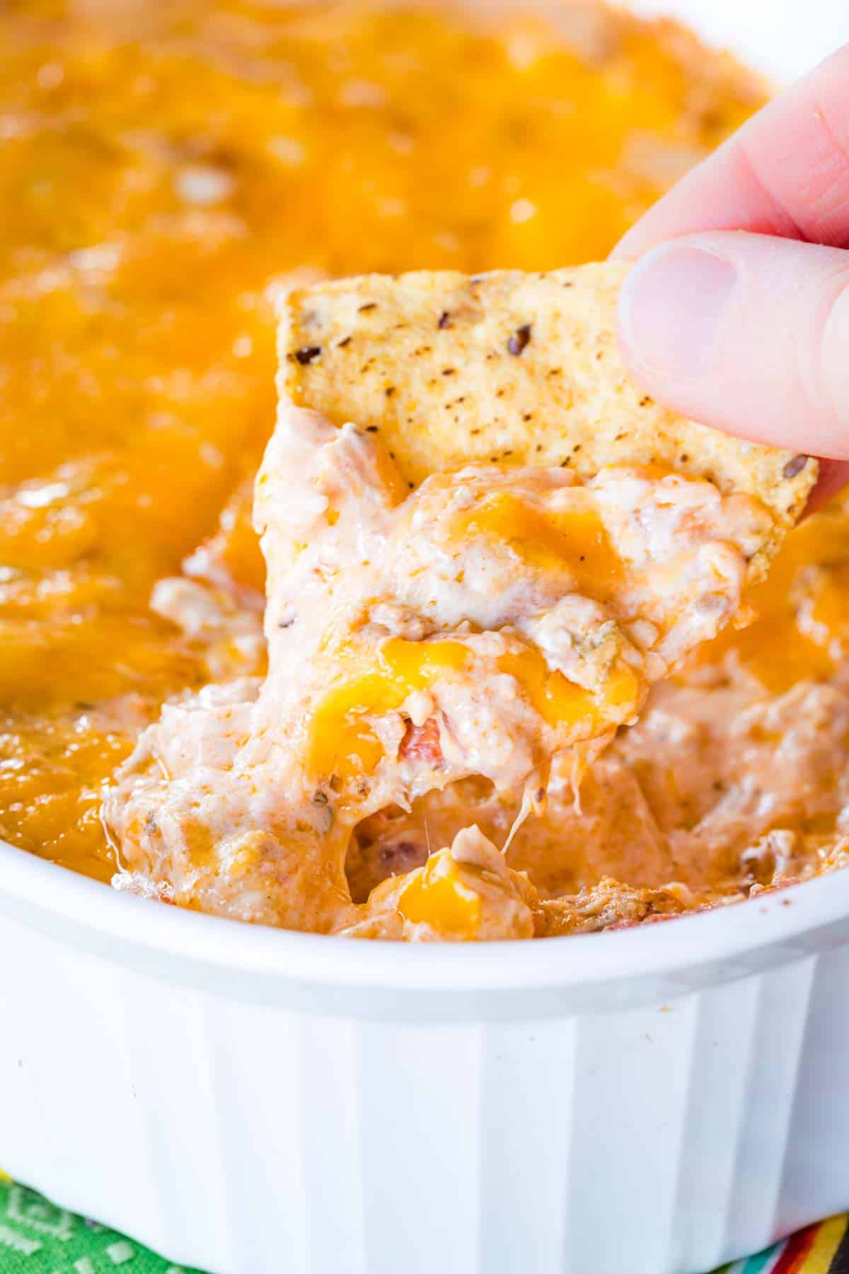 Cheesy dip being scooped out of a casserole dish with a tortilla chip.