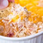 A tortilla chip being used to scoop up hot jambalaya dip.