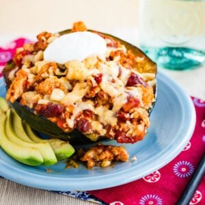 A chili stuffed acorn squash top with cheese and sour cream on a blue plate.