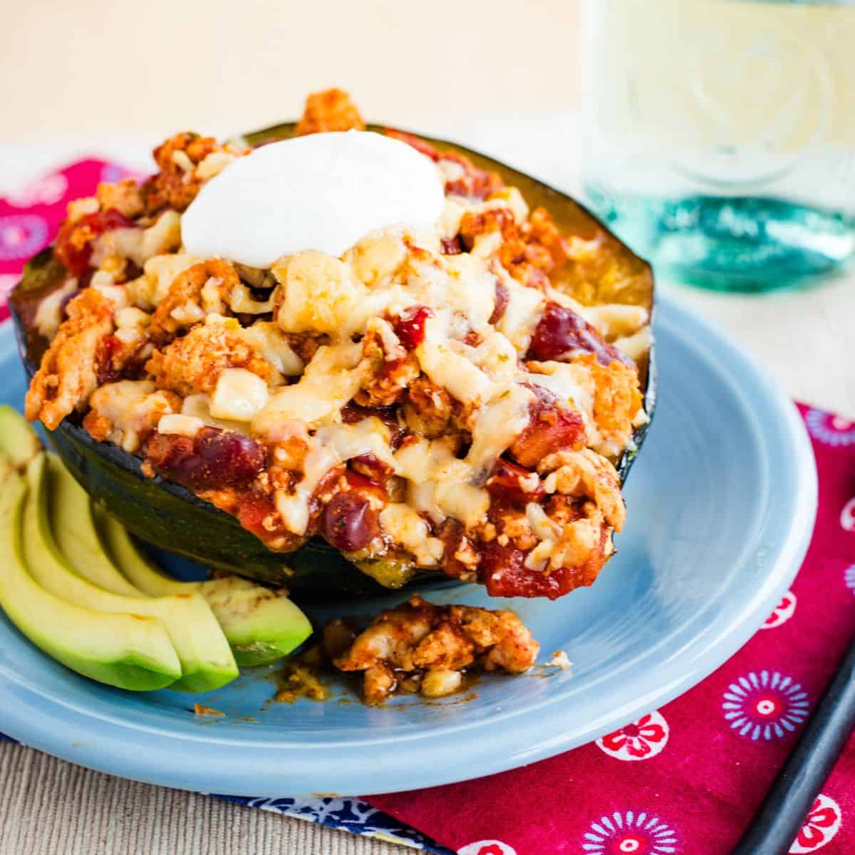 A chili stuffed acorn squash top with cheese and sour cream on a blue plate.