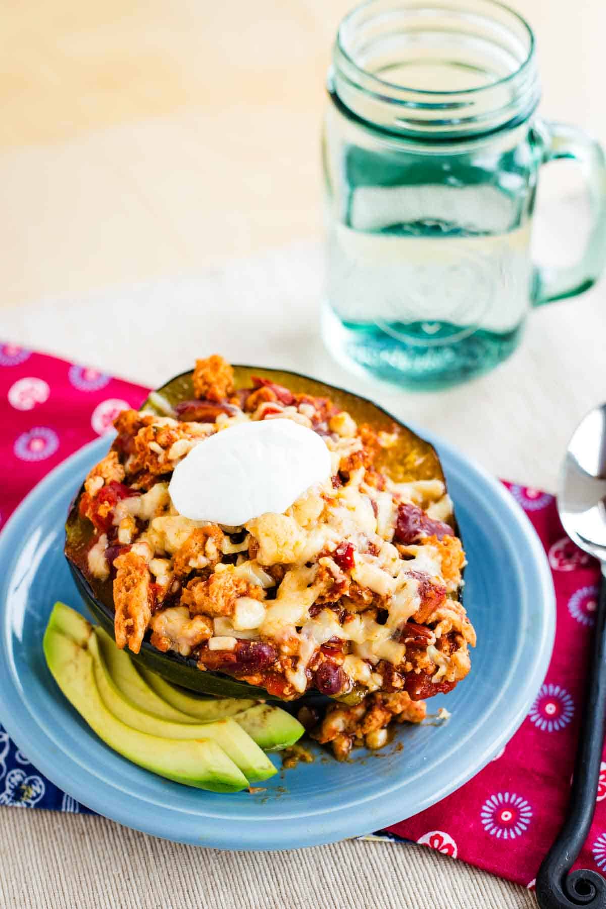 Half of a roasted acorn squash filled with chili talked with melted cheese and sour cream.