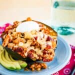 A turkey chili stuffed acorn squash half on a plate with some slices of avocado.