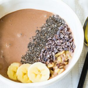 A close-up of a chocolate banana smoothie bowl with nuts cacao nibs and chia seeds on top.