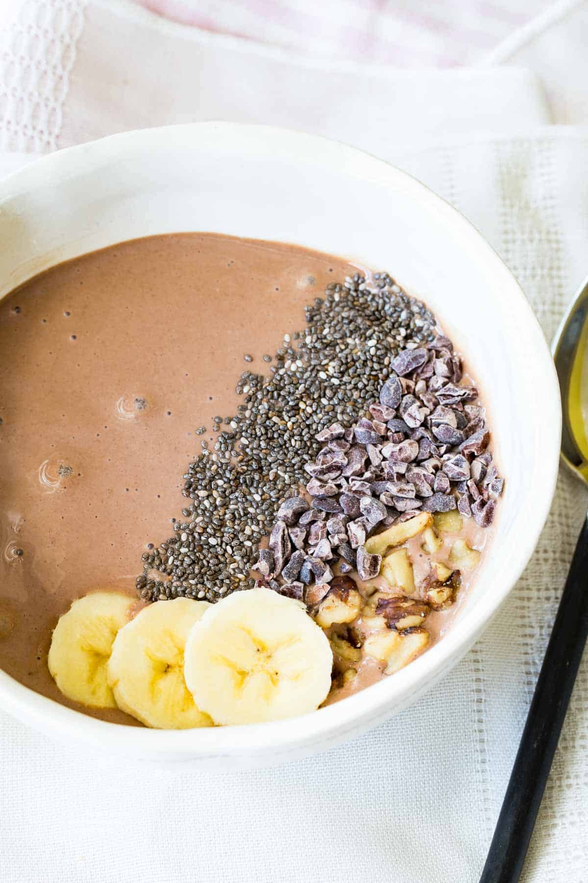 Looking down into a chocolate banana smoothie bowl with chopped walnuts Chia seeds and cacao nibs on top.
