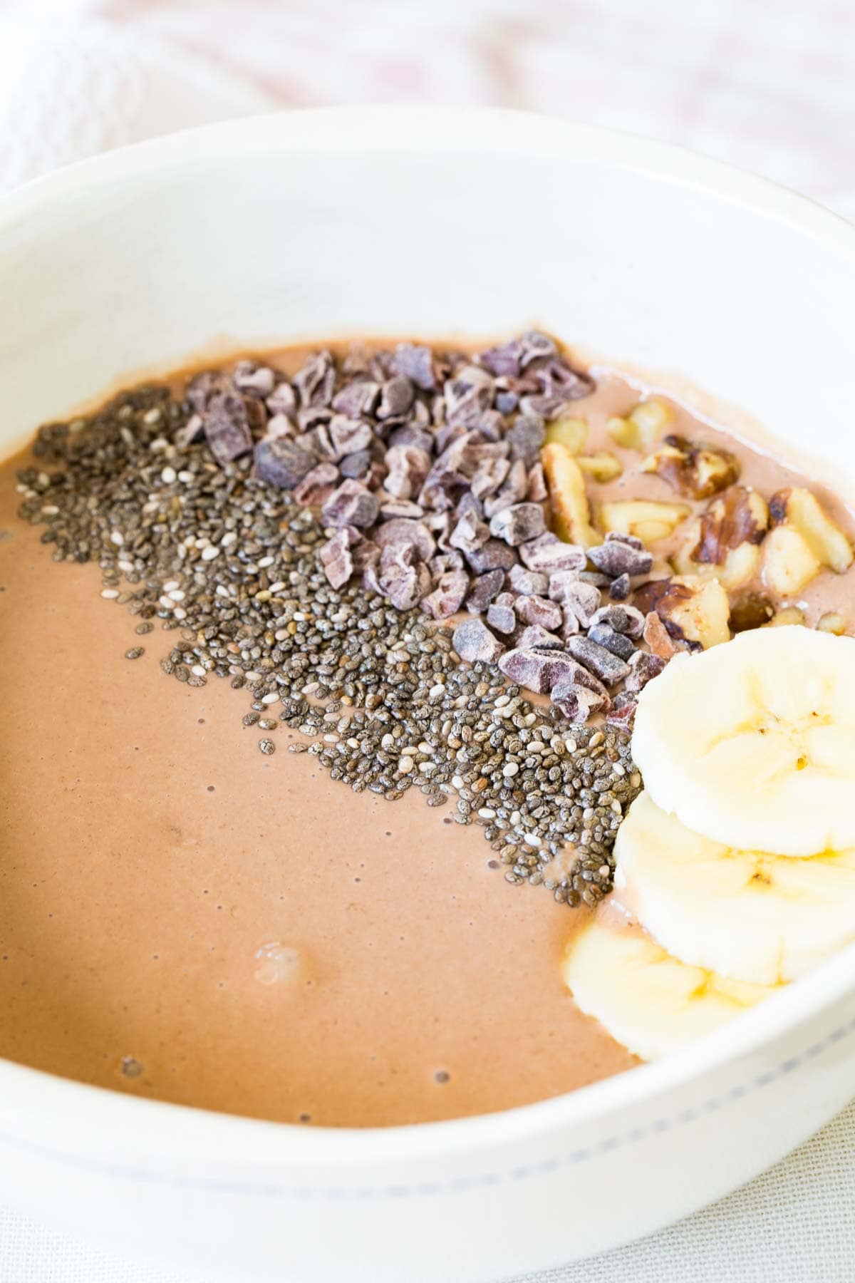 Chocolate smoothie bowl topped with banana slices Chia seeds cacao nibs and chopped walnuts.