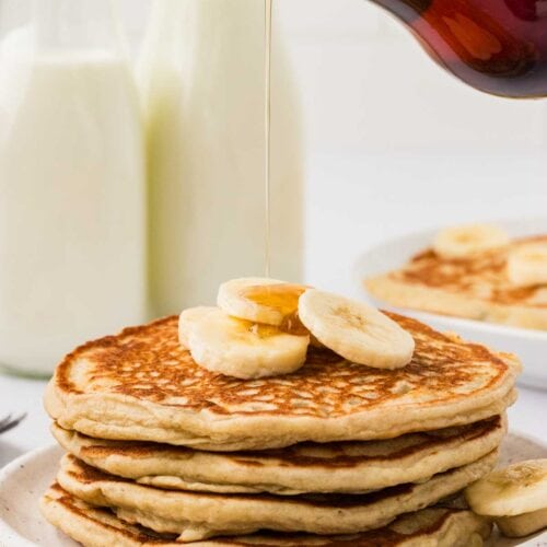 Syrup held over a plate of gluten free banana pancakes