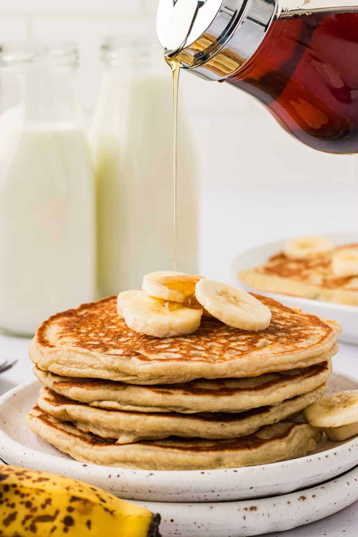 Syrup held over a plate of gluten free banana pancakes