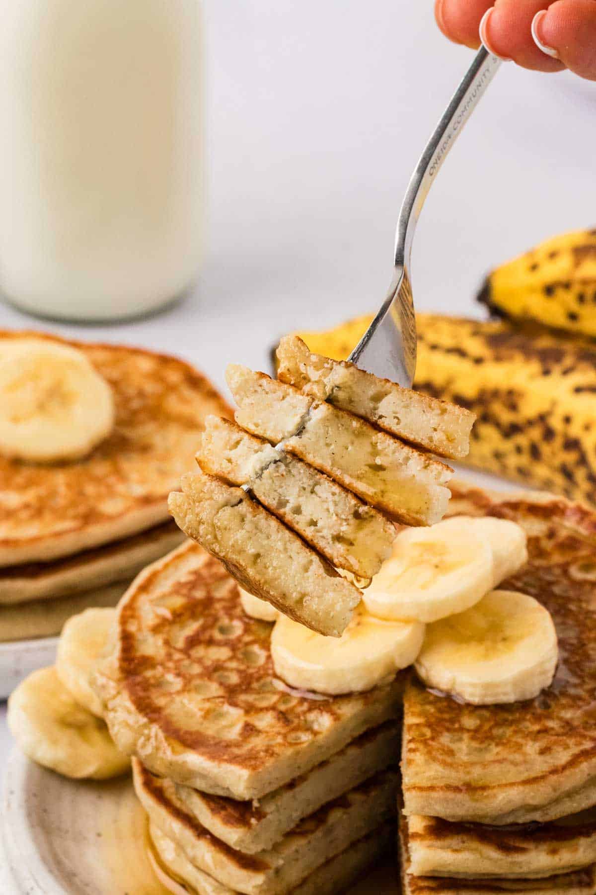 A forkful of banana pancakes held over the plate