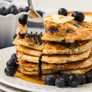 A stack of blueberry pancakes with a fork taking a bite
