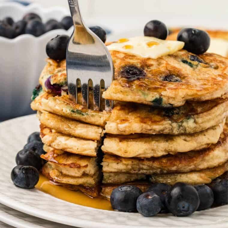 A stack of blueberry pancakes with a fork taking a bite