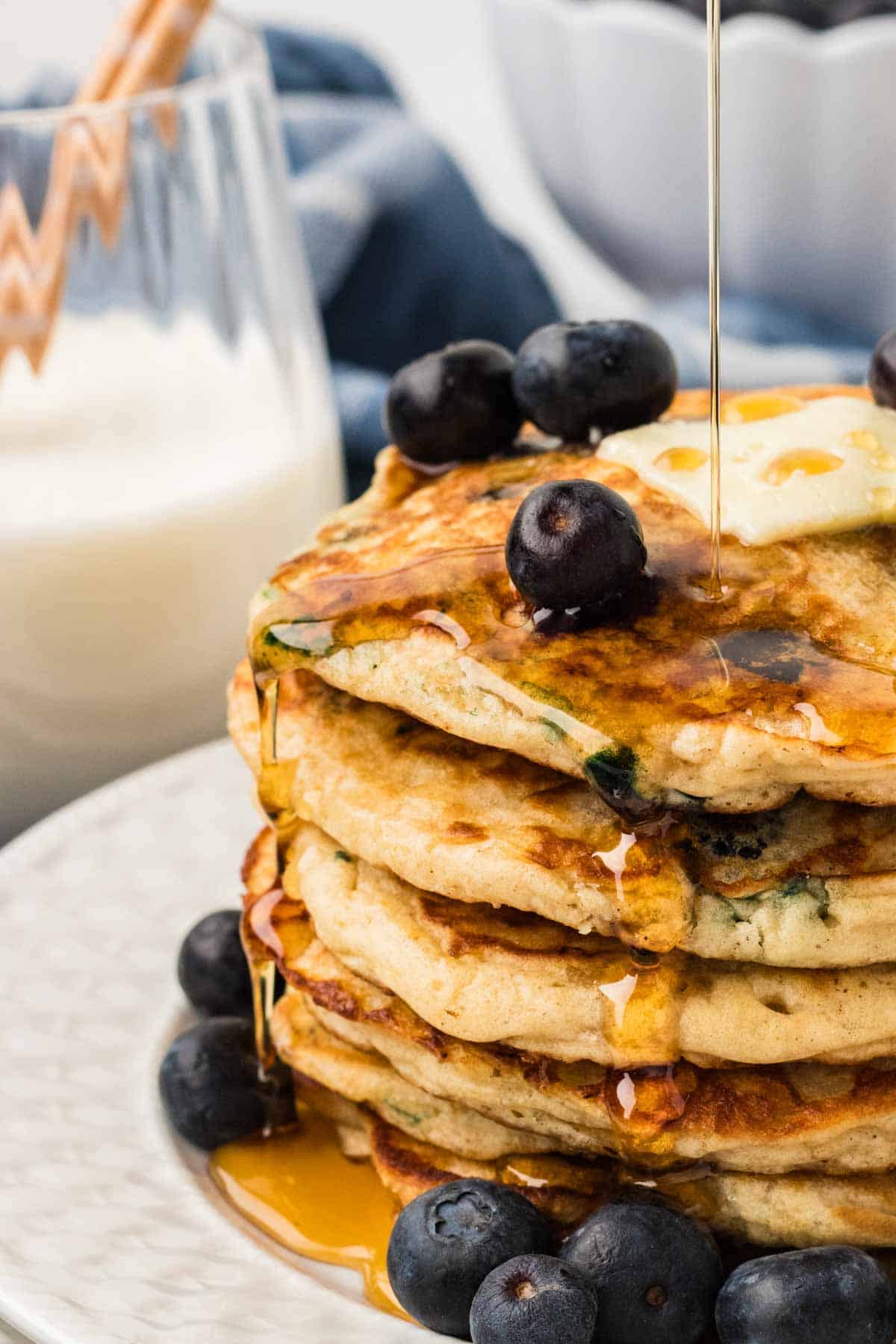 Syrup drizzling down the sides of a stack of gluten free blueberry pancakes
