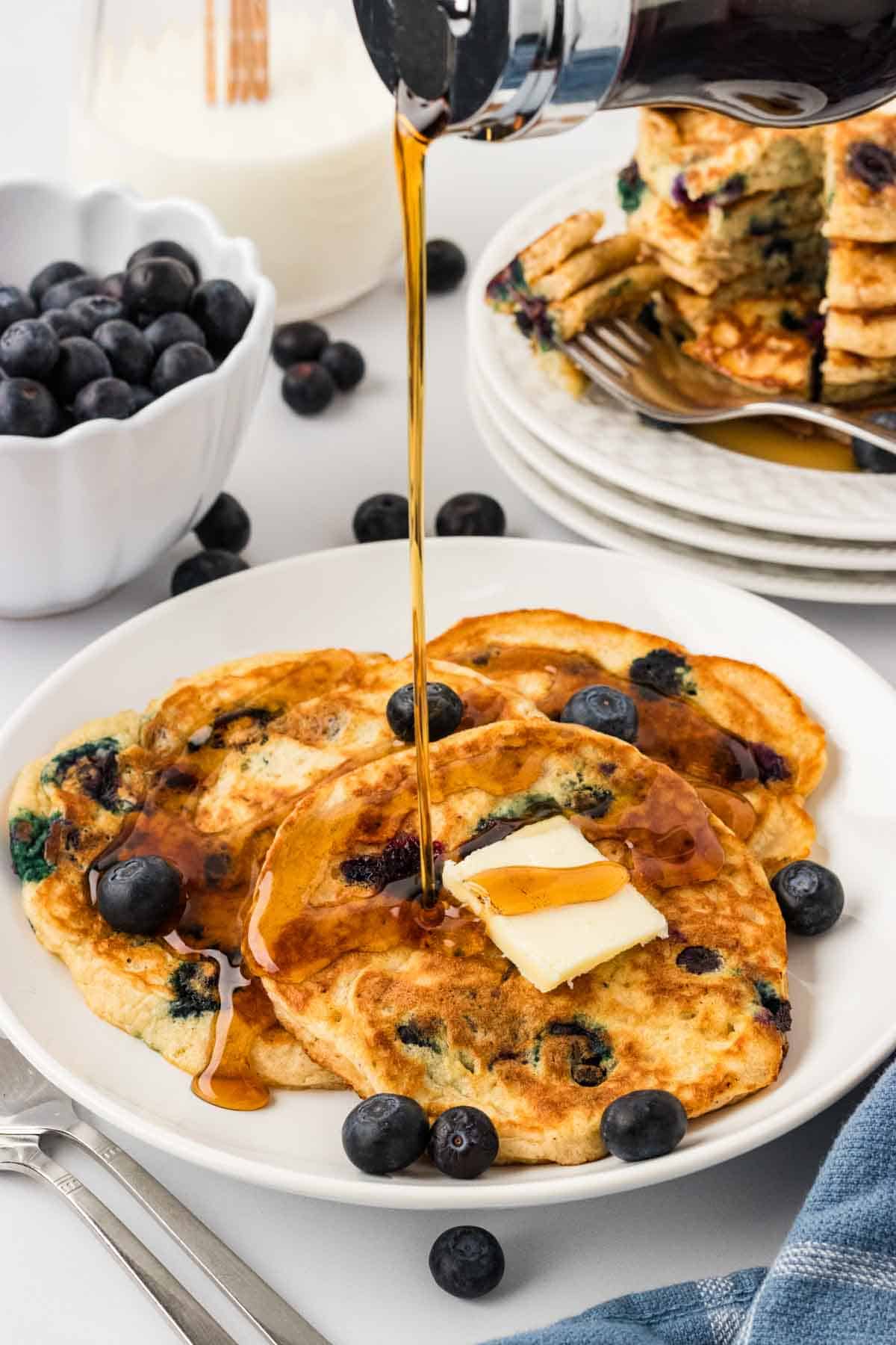 Drizzling syrup over a plate of gluten free blueberry pancakes
