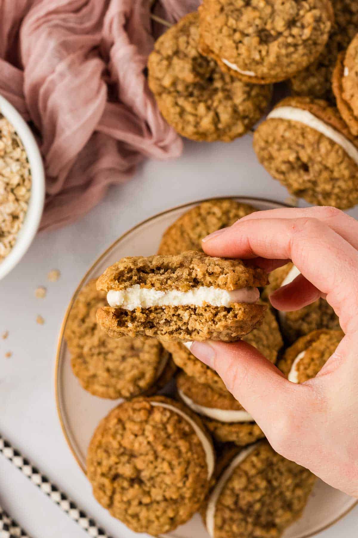 A hand holding an oatmeal cream pie with a bite missing