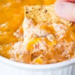 A chip being used to scoop up a melty dip with text overlay that says "Hot & Cheesy Jambalaya Dip".