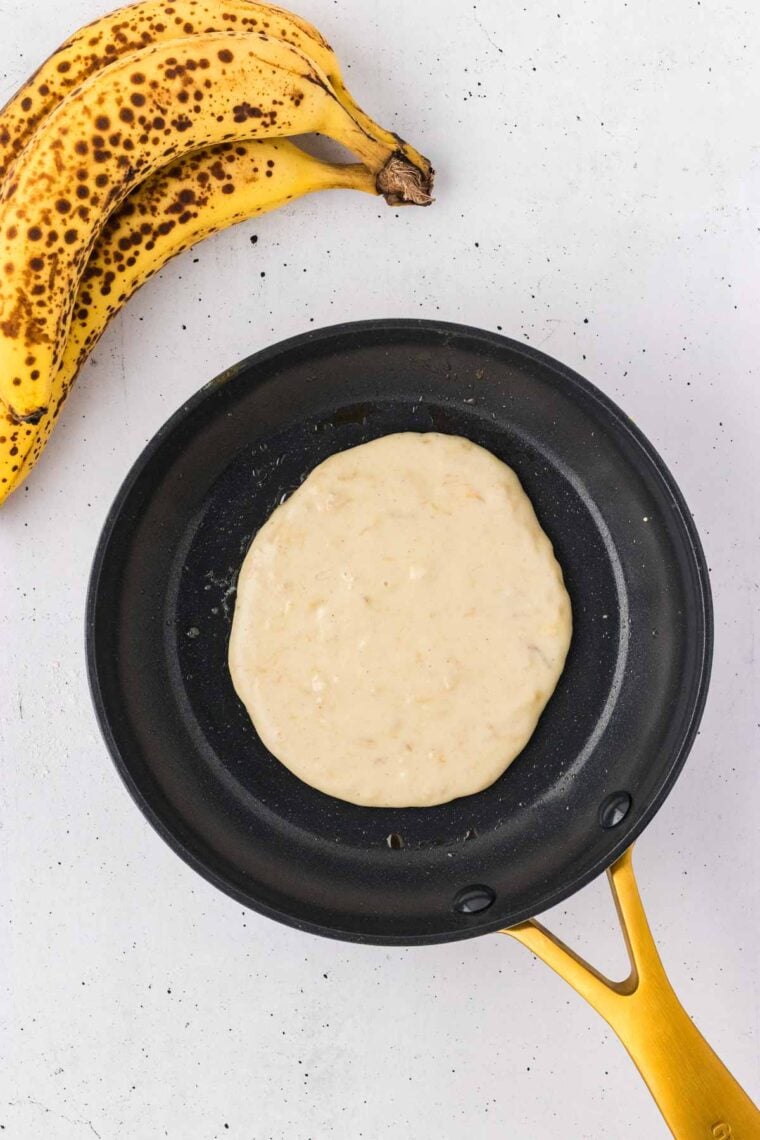 A banana pancake cooking in a skillet